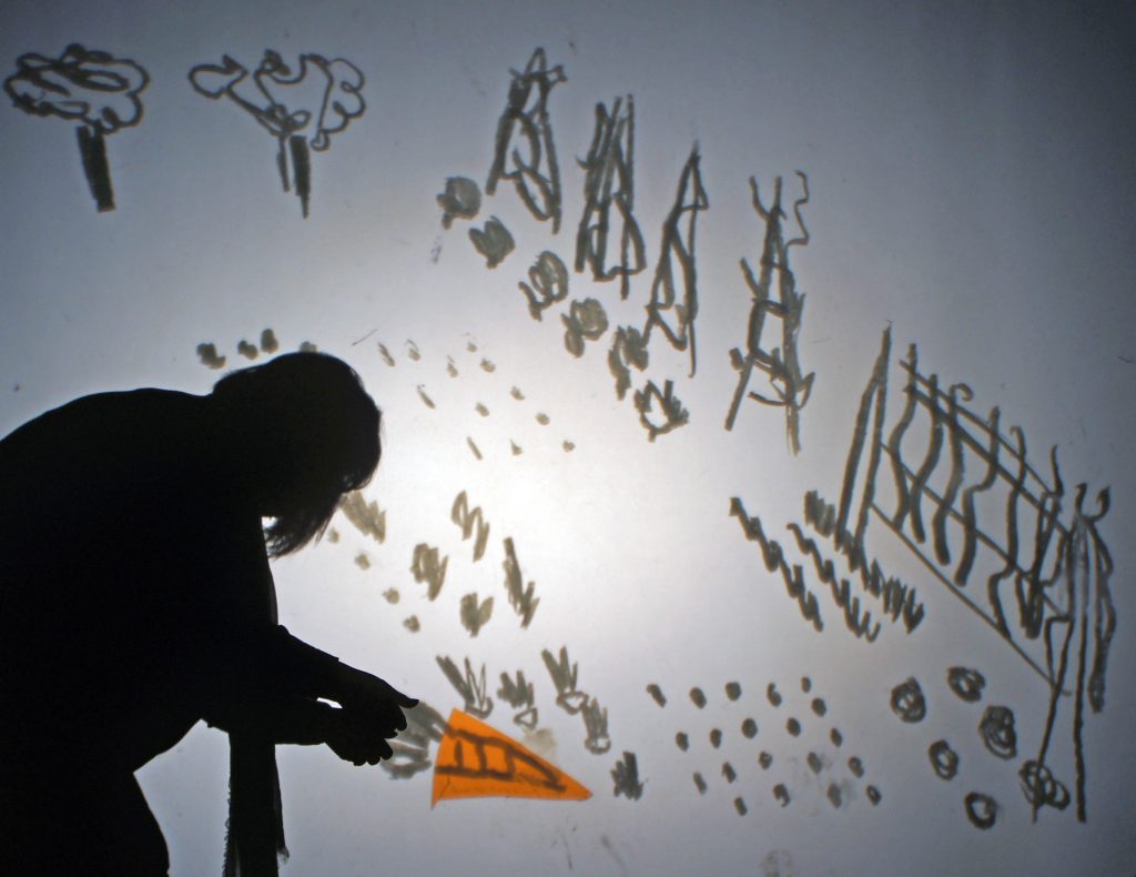Silhouette of an adult pulling an orange carrot out of a hand drawn vegetable garden in a shadow theatre scene